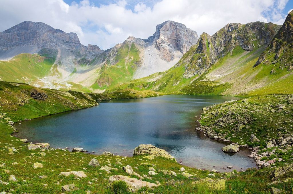 A turquoise glacier lake nestled in a green mountain valley beneath rocky peaks.