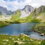 A turquoise glacier lake nestled in a green mountain valley beneath rocky peaks.