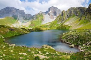 A turquoise glacier lake nestled in a green mountain valley beneath rocky peaks.